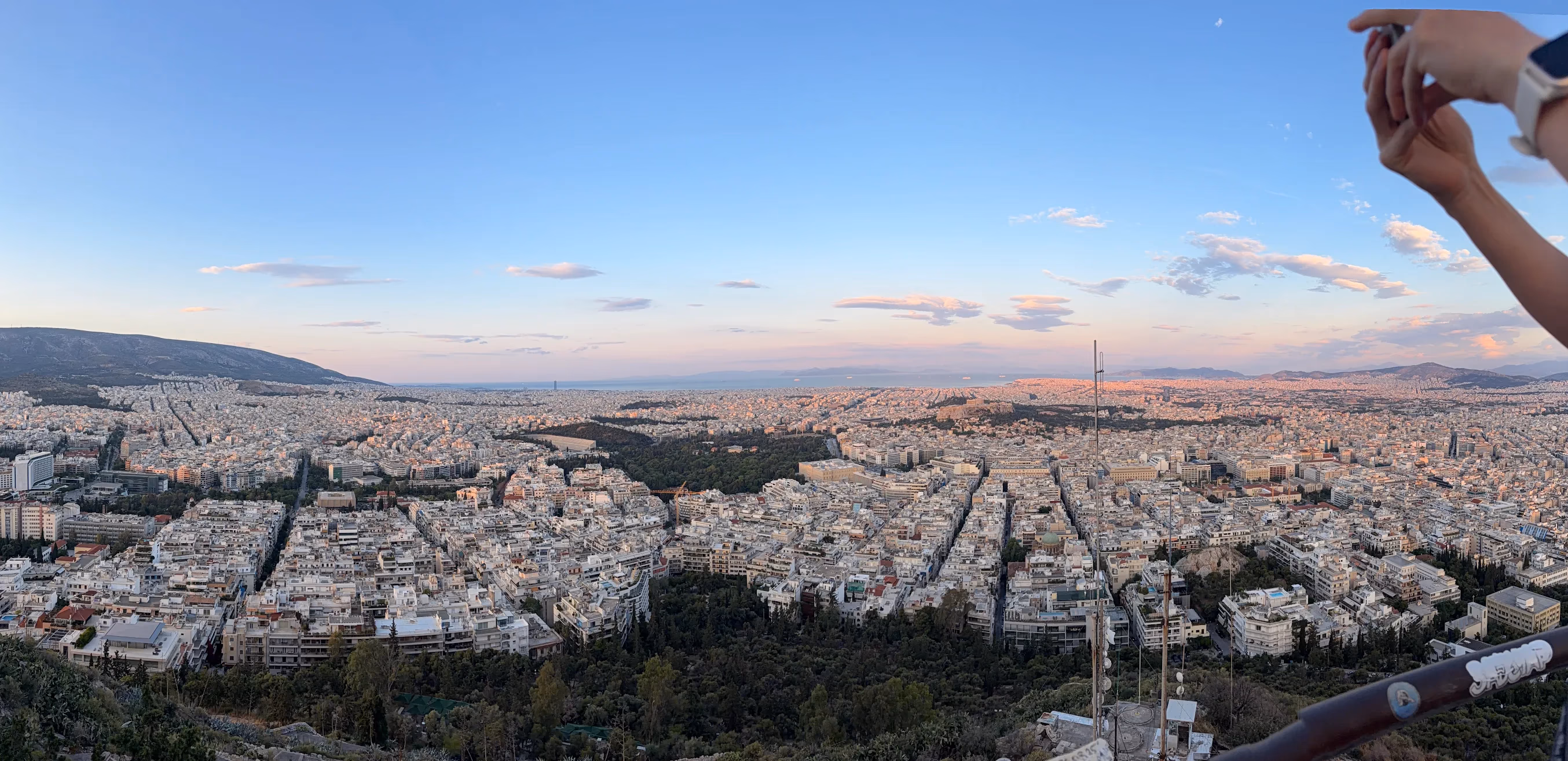 Wide panorama over Athens at dusk from the summit of Lycabettus Hill, the city stretching to the mountains