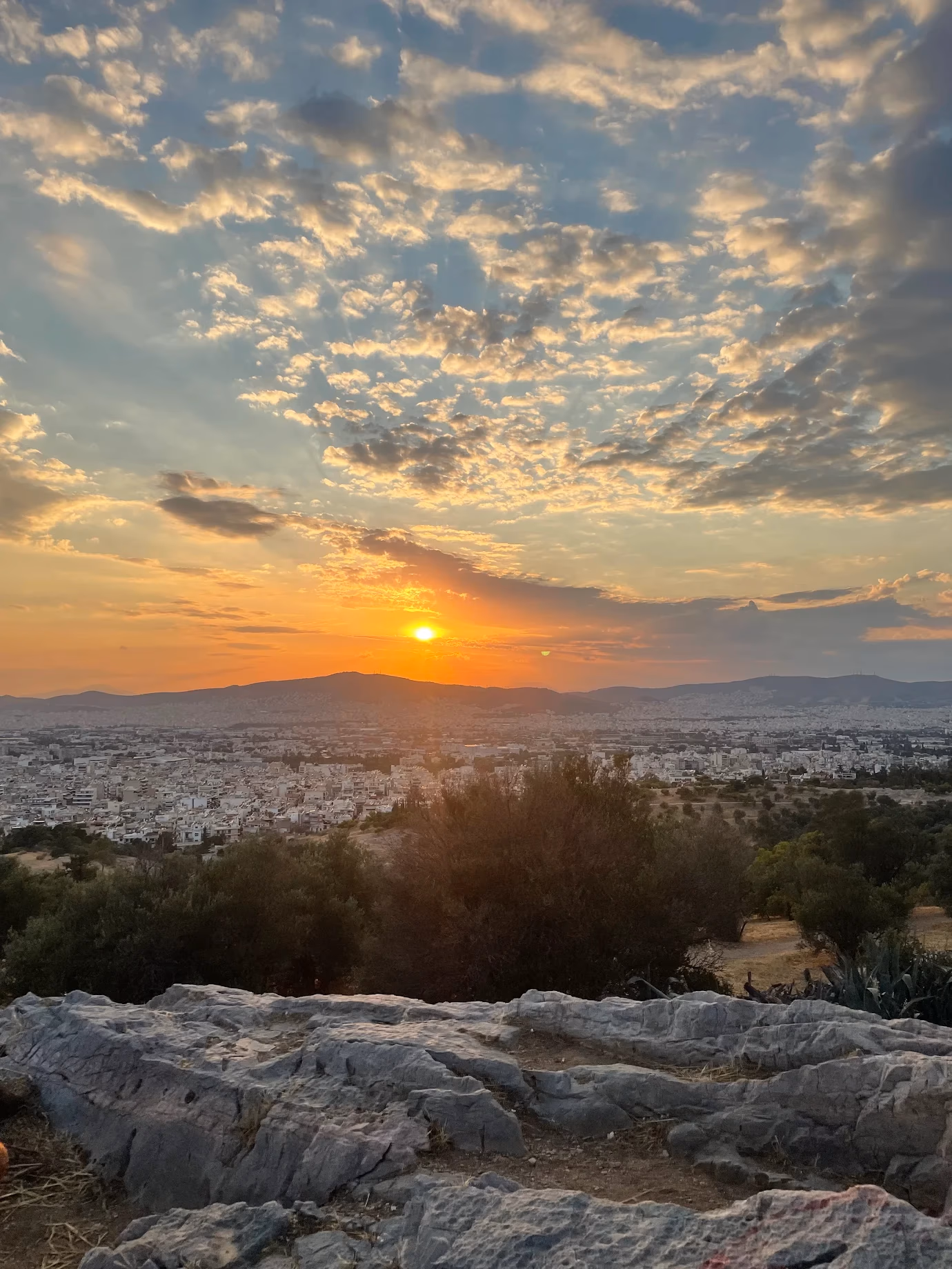 A vivid orange sunset over Athens seen from the rocks of Philopappos Hill