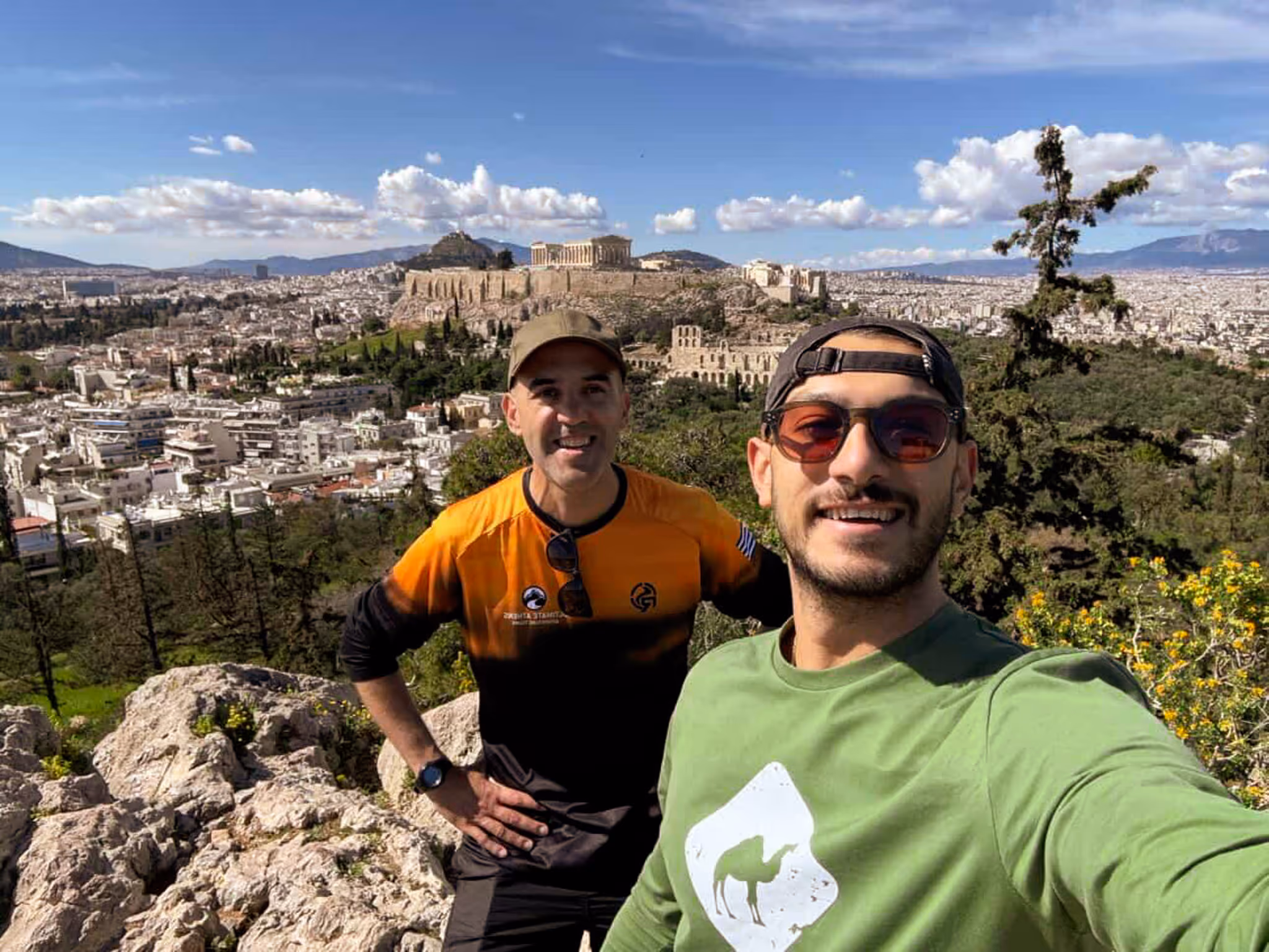 George and a guest at the Philopappos Hill viewpoint, the Acropolis and Parthenon across the valley behind them