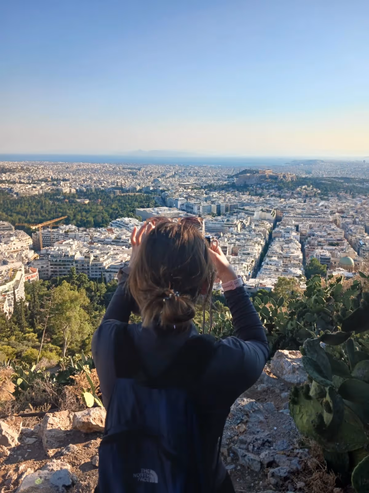 A guest photographing the Athens skyline from a hilltop viewpoint on Philopappos Hill